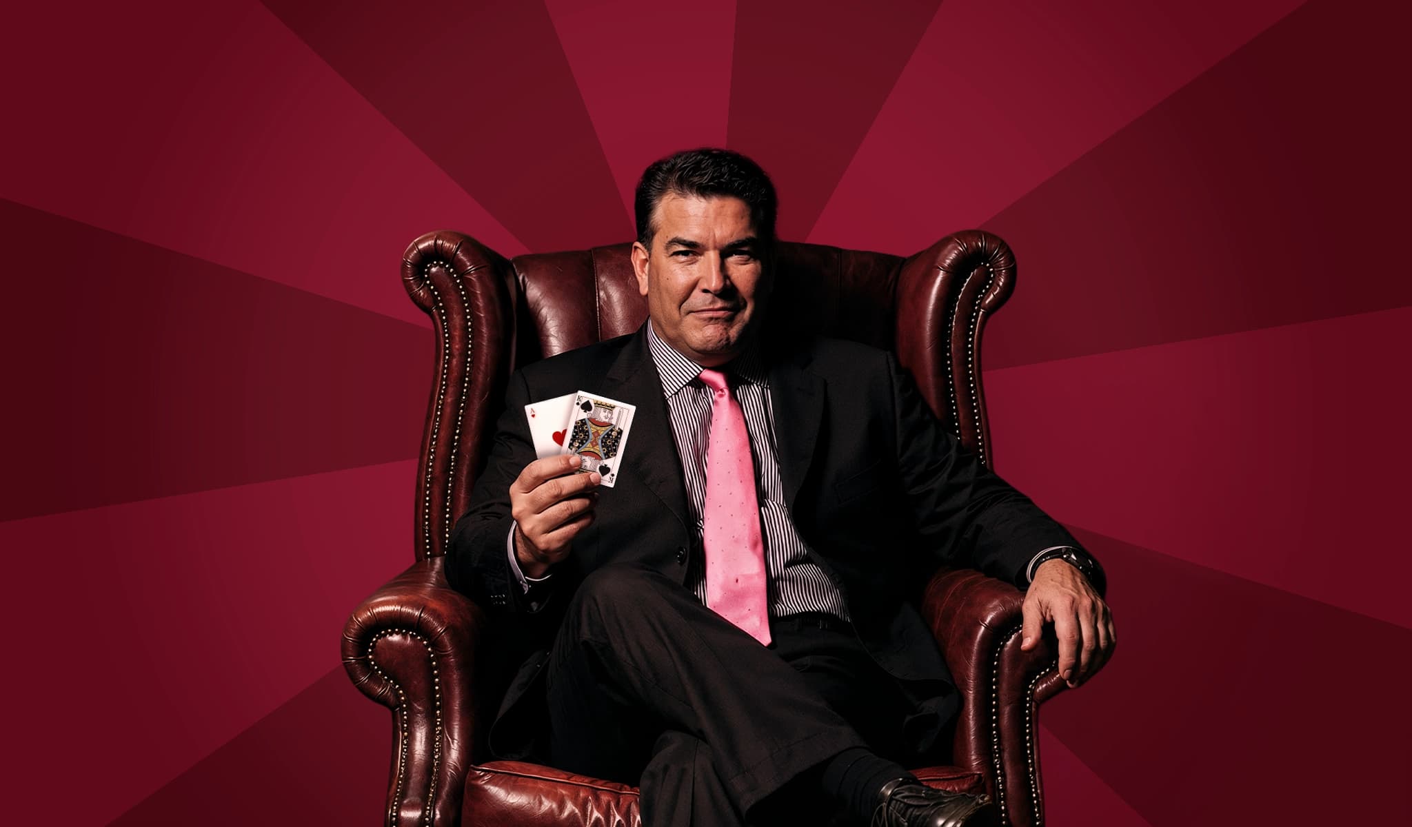 Don Johnson, blackjack legend, seated in a leather armchair holding playing cards including an ace.