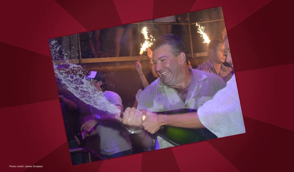 Don Johnson laughing as champagne sprays at a nightclub celebration with sparklers in the background.