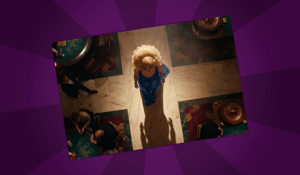 Overhead view of a person in a blue sequined dress and blonde wig walking through a casino floor surrounded by gaming tables