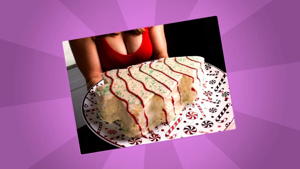 Christmas tree-shaped cake covered in white icing, red garland piping, and green sprinkles, held on a festive plate by a woman wearing a red top.