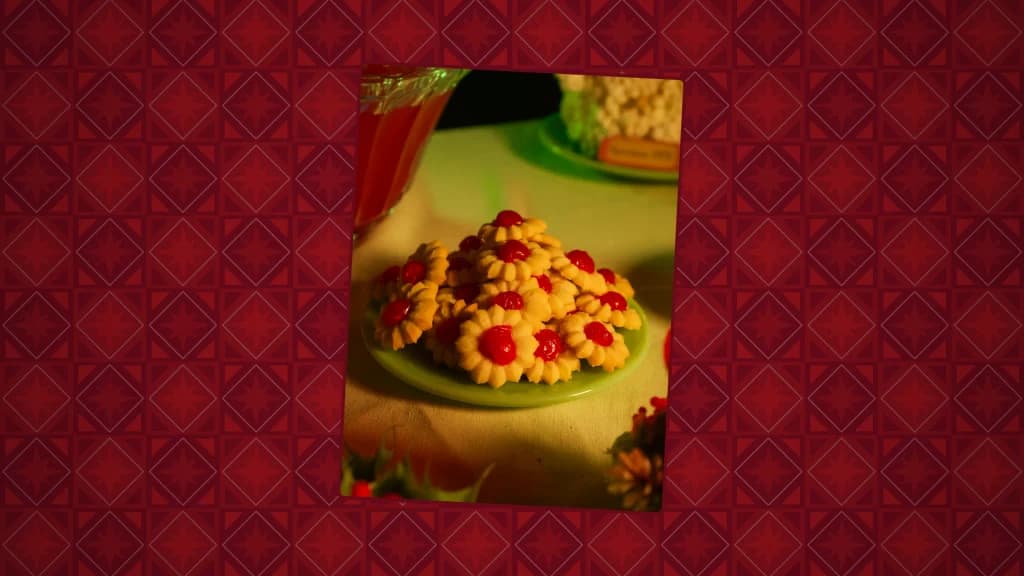A plate of flower-shaped cherry spritz cookies topped with maraschino cherries on a holiday table.