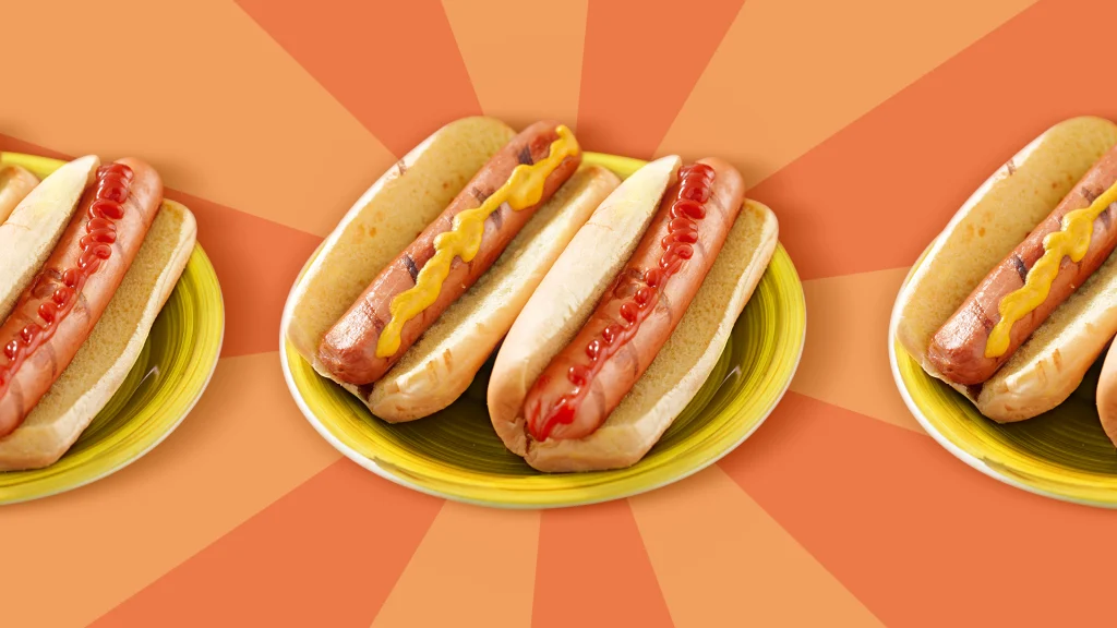 We see two large hotdogs sitting inside buns, one with ketchup and the other with mustard, placed on a yellow plate.