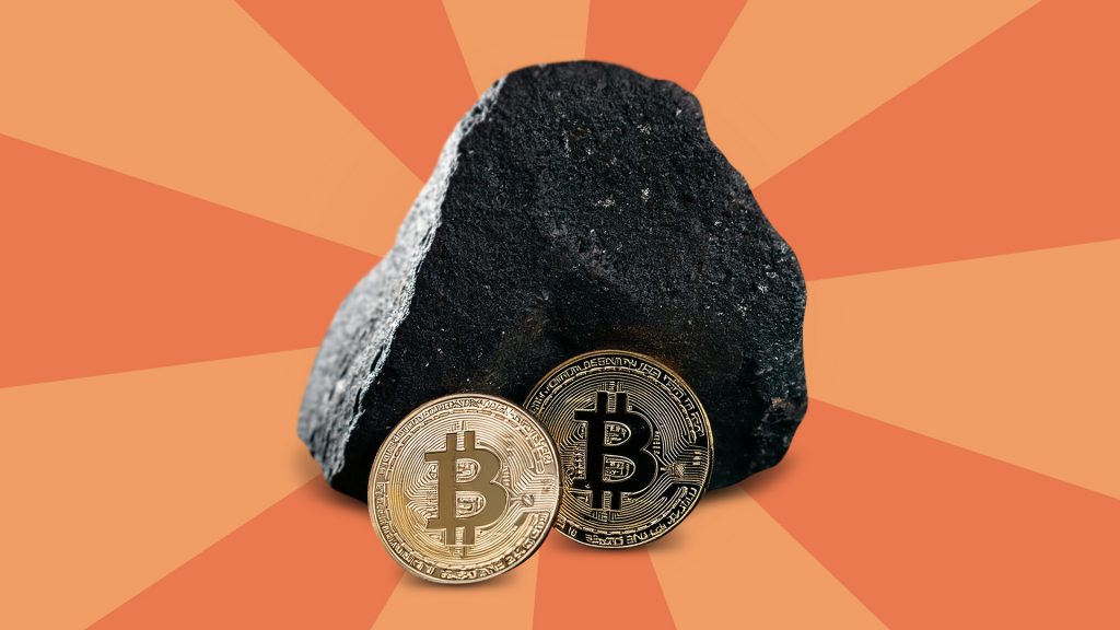 Two shiny Bitcoins rest against a big black rock on a two-toned peach background. 