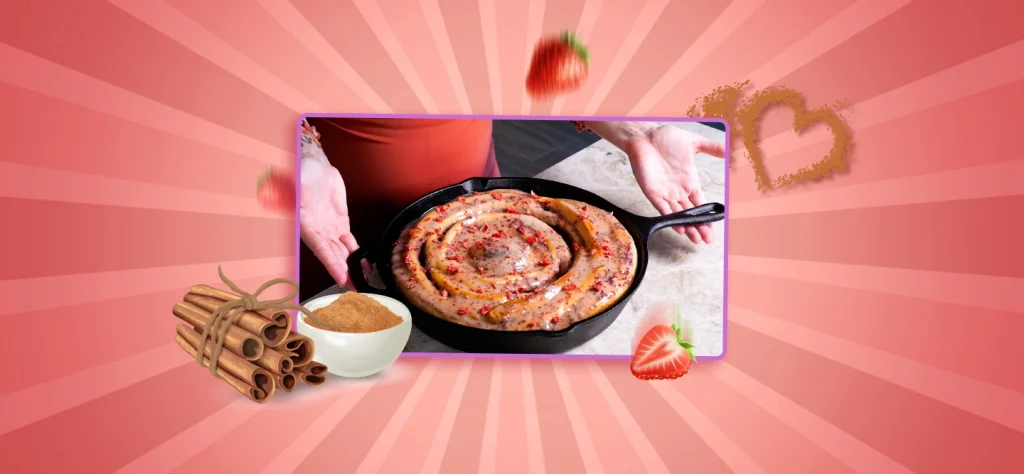 On a pink back ground with cinnamon sticks and strawberries is an image of hunger diairies strawberry cinnamon roll in a cast iron pan