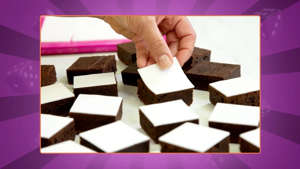 A hand places white fondant on top of evenly cut square brownies