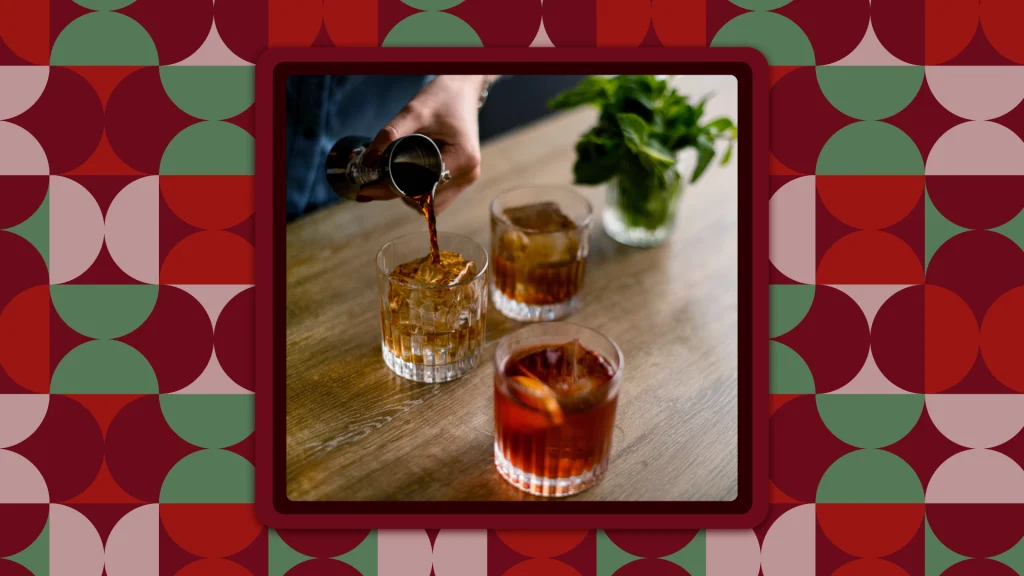 John Rondi’s hand is pouring Blanco Tequila from a chrome shot glass into a glass tumbler that is set on a wooden table adjacent to two other glass tumblers with alcohol.